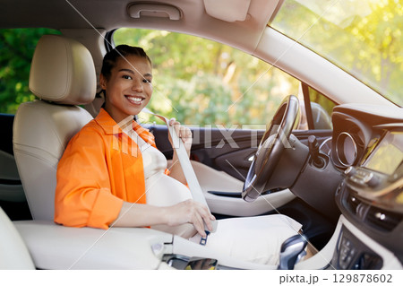 Black pregnant woman fastening seatbelt before driving, smiling confidently Black pregnant woman fastening seatbelt before driving, smiling confidently 129878602
