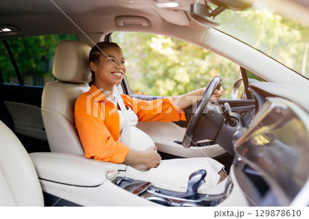 Young African American pregnant woman joyfully driving car, hand on belly 129878610
