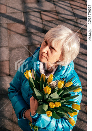 woman holding yellow tulips while looking up in sunny outdoor setting. closeup. woman holding yellow tulips while looking up in sunny outdoor setting. closeup. 129879092
