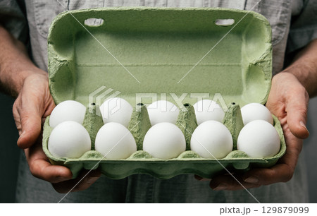hands hold carton ten white eggs in green container in kitchen setting fresh groceries. closeup. hands hold carton ten white eggs in green container in kitchen setting fresh groceries. closeup. 129879099