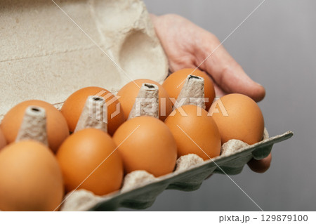 hand holding an egg carton with fresh brown eggs in kitchen setting. closeup. hand holding an egg carton with fresh brown eggs in kitchen setting. closeup. 129879100