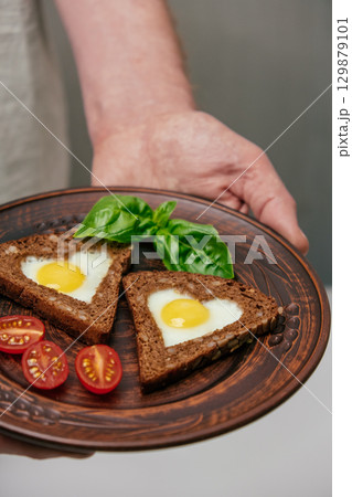 delicious breakfast feature eggs in toast served cherry tomatoes, basil on rustic plate. closeup. delicious breakfast feature eggs in toast served cherry tomatoes, basil on rustic plate. closeup. 129879101