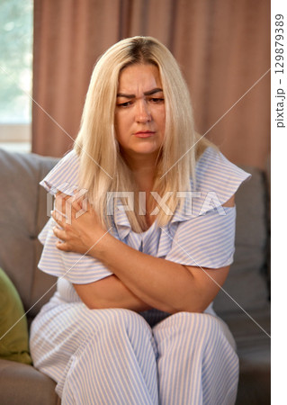 Blonde woman holding shoulder with worried expression Blonde woman holding shoulder with worried expression 129879389