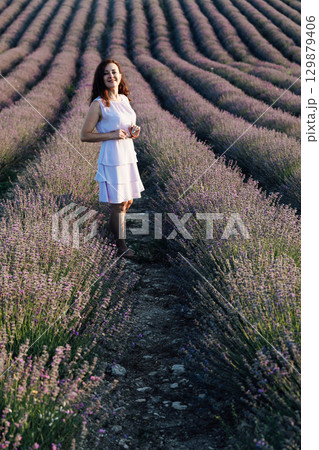 woman in a white summer dress on a lavender field smiling 129879406