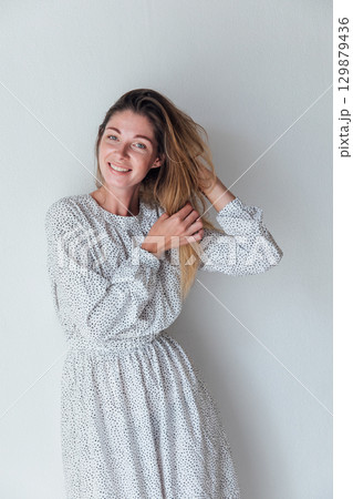 woman in white summer dress smiling and touching hair 129879436