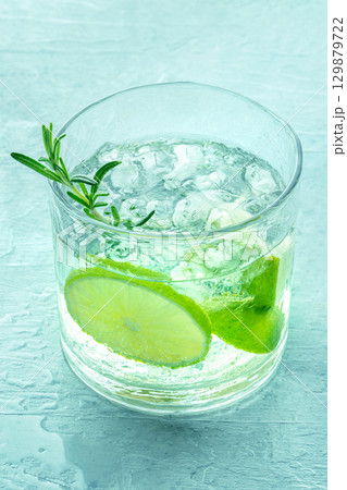 Gin tonic, a glass of gin with soda, lime, rosemary, and ice, on blue Gin tonic, a glass of gin with soda, lime, rosemary, and ice, on blue 129879722