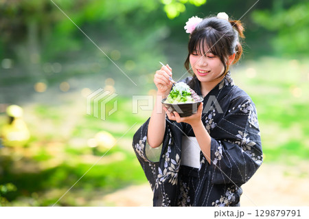 高原の湖で浴衣を着た日本人の小学生の女の子がかき氷を食べている風景 129879791