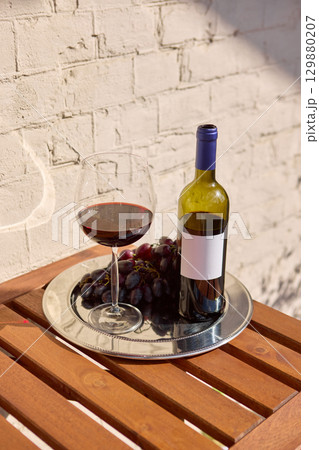 Red wine bottle with blank label with grapes and glass on tray outdoor setting 129880207