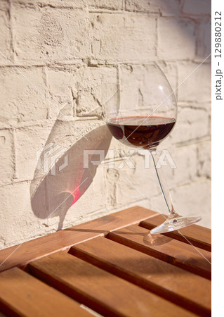 Red wine glass with shadow on wall and wooden table 129880212