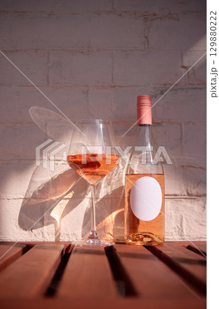 Rose wine bottle with blank label next to glass on wooden table against brick wall Rose wine bottle with blank label next to glass on wooden table against brick wall 129880222