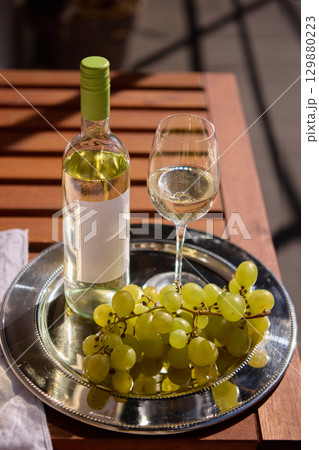 White wine bottle with blank label with grapes and glass on wooden table 129880223