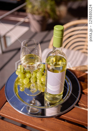Bottle of white wine with blank label, with grapes on silver tray, mockup for ad, text 129880224