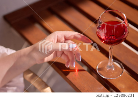 Female hand with glass of red wine on wooden table Female hand with glass of red wine on wooden table 129880231