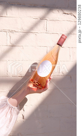 Rose wine bottle with blank round label in hand against brick wall, mockup for ad, text 129880238