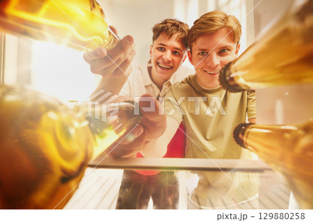Two smiling young men reaching for beer bottles from fridge view 129880258