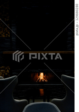 Cozy living room with a modern stone fireplace, warm flames flickering inside, creating an inviting and tranquil atmosphere. Cozy living room with a modern stone fireplace, warm flames flickering inside, creating an inviting and tranquil atmosphere. 129880280