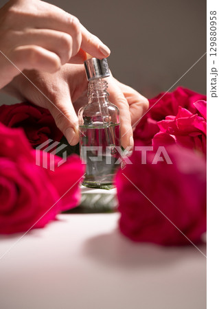 Hands Preparing to Dispense Liquid From a Glass Bottle Surrounded by Fresh Roses 129880958