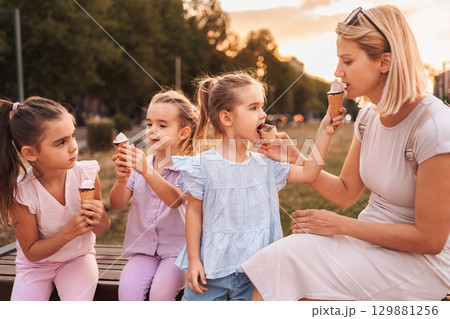 Mother and daughters enjoying ice cream cones in a park at sunset 129881256
