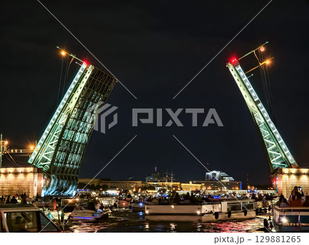 Nighttime view of a drawbridge in St. Petersburg opening over a river with boats passing in the foreground Nighttime view of a drawbridge in St. Petersburg opening over a river with boats passing in the foreground 129881265