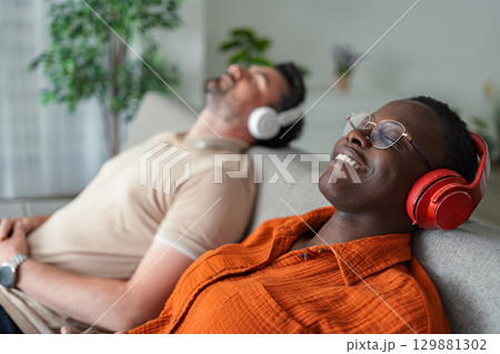 Couple relaxing on sofa listening to music with headphones Couple relaxing on sofa listening to music with headphones 129881302