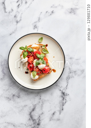 Caprese sandwich or toast with mozzarrella balls, cherry tomatoes, olive oil and fresh basil leaves top view, isolated. Healthy vegetarian breakfast. White marble background 129881710