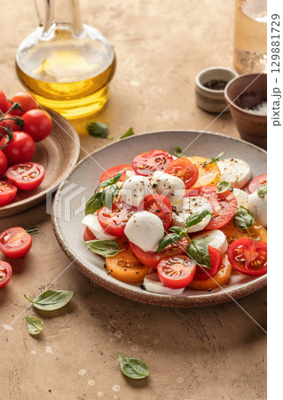 Caprese salad with sliced tomatoes, mozzarella, basil, olive oil on brown textured background 129881729