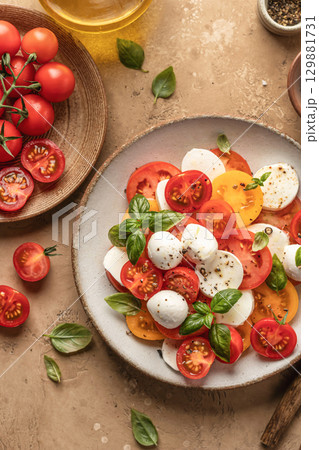 Caprese salad with sliced tomatoes, mozzarella, basil, olive oil close up on brown textured background. Top view Caprese salad with sliced tomatoes, mozzarella, basil, olive oil close up on brown textured background. Top view 129881731