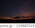 Late twilight view of a flooded rice field under a darkening sky. Clouds drift across deep purple and orange hues, with silhouettes of hills and trees adding a calm, moody atmosphere. 129882318