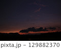 A moody twilight landscape featuring dark cloud shapes against a fading orange and purple sky. Silhouettes of distant hills and flooded rice fields evoke a calm rural scene. 129882370