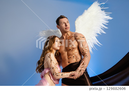 Couple posing with artistic wings against a blue backdrop in a creative studio 129882606