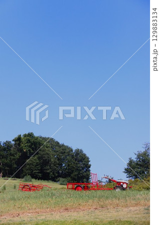 夏の青空と丘の上に置かれた赤い農耕車の里山風景 129883134