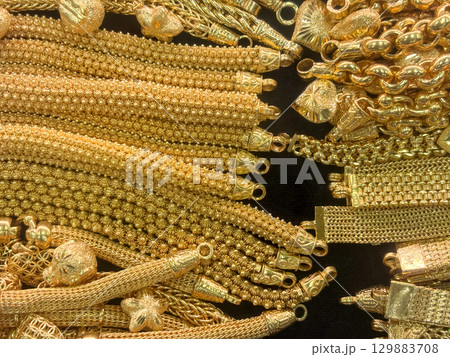 An extensive array of intricate gold bracelet is meticulously arranged on a dark surface, showcasing various style and texture in a lively marketplace atmosphere during the day. An extensive array of intricate gold bracelet is meticulously arranged on a dark surface, showcasing various style and texture in a lively marketplace atmosphere during the day. 129883708