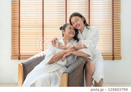 In a cozy spa, a mother and daughter share joyful moment wrapped in soft robe, surrounded by natural light and wooden texture. In a cozy spa, a mother and daughter share joyful moment wrapped in soft robe, surrounded by natural light and wooden texture. 129883799