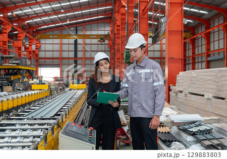 Two worker with safety helmet and black suit standing in a factory, holding clipboard, used for taking note, check schedule and review document. 129883803