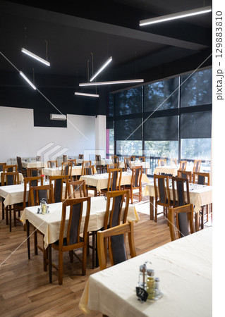 Restaurant interior with large sunlit windows and wooden chairs Restaurant interior with large sunlit windows and wooden chairs 129883810