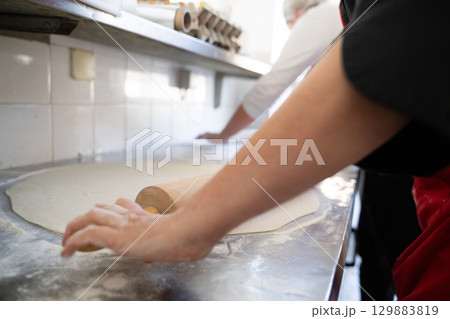 Rolling out dough on floured surface in commercial kitchen Rolling out dough on floured surface in commercial kitchen 129883819