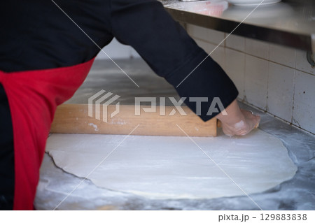 Rolling out dough on floured surface in commercial kitchen 129883838