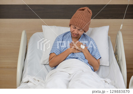 Patient in hospital bed experiencing discomfort while wearing a knitted cap in a healthcare setting 129883870