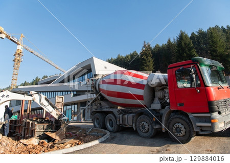 The exterior of a business building under construction is surrounded by trucks, cranes, and various construction materials, creating a bustling scene of an expansive industrial worksite in progress The exterior of a business building under construction is surrounded by trucks, cranes, and various construction materials, creating a bustling scene of an expansive industrial worksite in progress 129884016