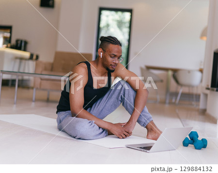 Training At Home. Sporty man doing the training while watching an online tutorial on a laptop, exercising in the living room, free space. Training At Home. Sporty man doing the training while watching an online tutorial on a laptop, exercising in the living room, free space. 129884132