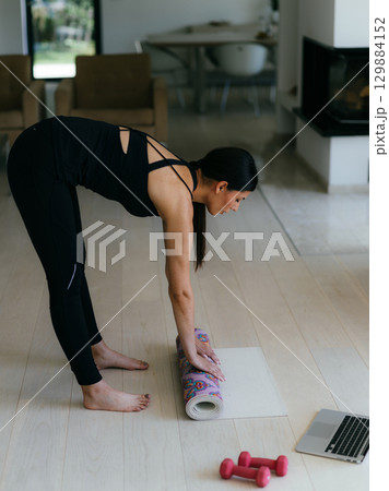 Woman in sports clothes preparing sports equipment for online training in her living room. Woman in sports clothes preparing sports equipment for online training in her living room. 129884152