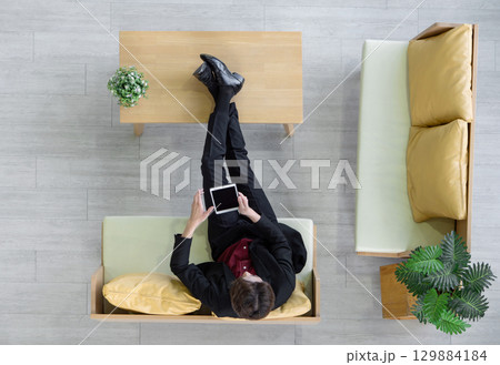 Young businessman in suit sit relax on sofa, rest his feet on the table while use tablet computer searching for interesting investment information. Top View 129884184