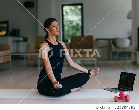 Young Beautiful Female Exercising, Stretching and Practising Yoga with Trainer via Video Call Conference in Bright Sunny House. Healthy Lifestyle, Wellbeing and Mindfulness Concept. Young Beautiful Female Exercising, Stretching and Practising Yoga with Trainer via Video Call Conference in Bright Sunny House. Healthy Lifestyle, Wellbeing and Mindfulness Concept. 129884393