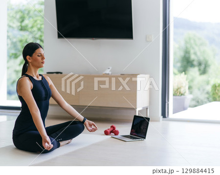 Young Beautiful Female Exercising, Stretching and Practising Yoga with Trainer via Video Call Conference in Bright Sunny House. Healthy Lifestyle, Wellbeing and Mindfulness Concept. Young Beautiful Female Exercising, Stretching and Practising Yoga with Trainer via Video Call Conference in Bright Sunny House. Healthy Lifestyle, Wellbeing and Mindfulness Concept. 129884415