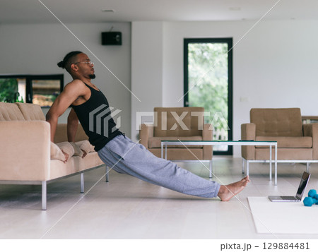 Training At Home. Sporty man doing the training while watching an online tutorial on a laptop, exercising in the living room, free space. Training At Home. Sporty man doing the training while watching an online tutorial on a laptop, exercising in the living room, free space. 129884481