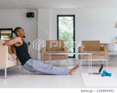 Training At Home. Sporty man doing the training while watching an online tutorial on a laptop, exercising in the living room, free space. Training At Home. Sporty man doing the training while watching an online tutorial on a laptop, exercising in the living room, free space. 129884482