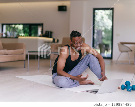 Training At Home. Sporty man doing the training while watching an online tutorial on a laptop, exercising in the living room, free space. Training At Home. Sporty man doing the training while watching an online tutorial on a laptop, exercising in the living room, free space. 129884489