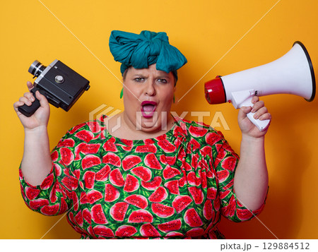 Plus size woman shouting with megaphone and holding vintage camera 129884512