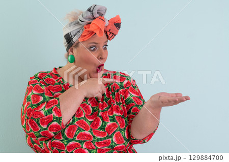 Surprised woman pointing at open hand in studio Surprised woman pointing at open hand in studio 129884700