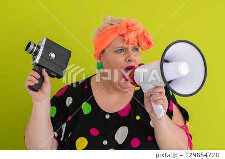 Woman shouting into megaphone and holding vintage camera 129884728